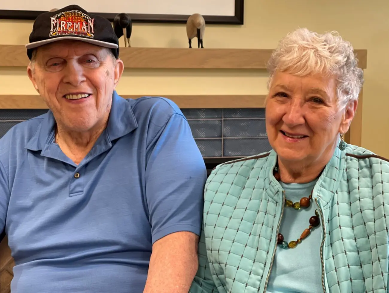 A couple posing for the camera, the woman has a turquoise jacket and the man has a fireman hat.
