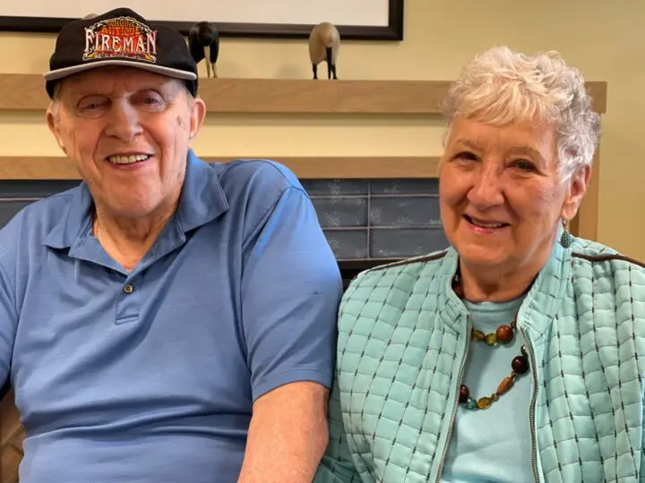 A couple posing for the camera, the woman has a turquoise jacket and the man has a fireman hat.