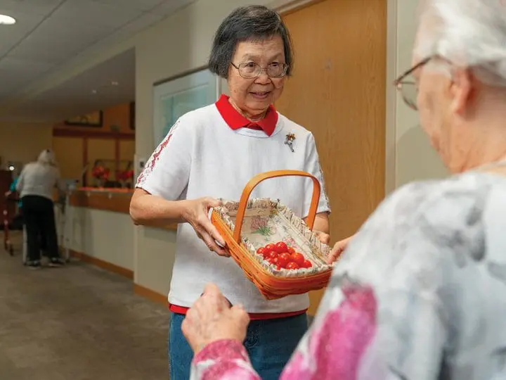 A caregiver offers fresh tomatoes to a resident, showcasing gratitude and friendship.