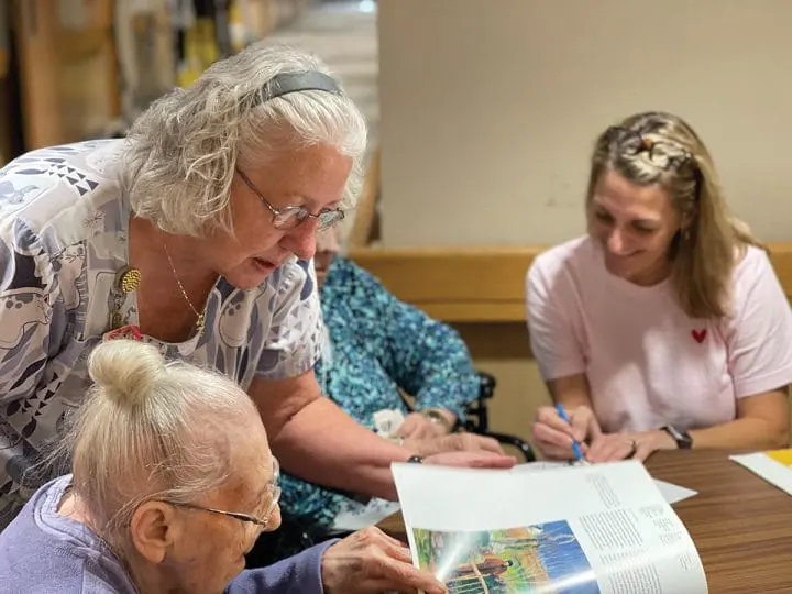 A caregiver assists a resident with their newspaper, showcasing nursing with heart.