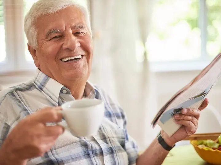 A man laughs as he reads a magazine and sips coffee.
