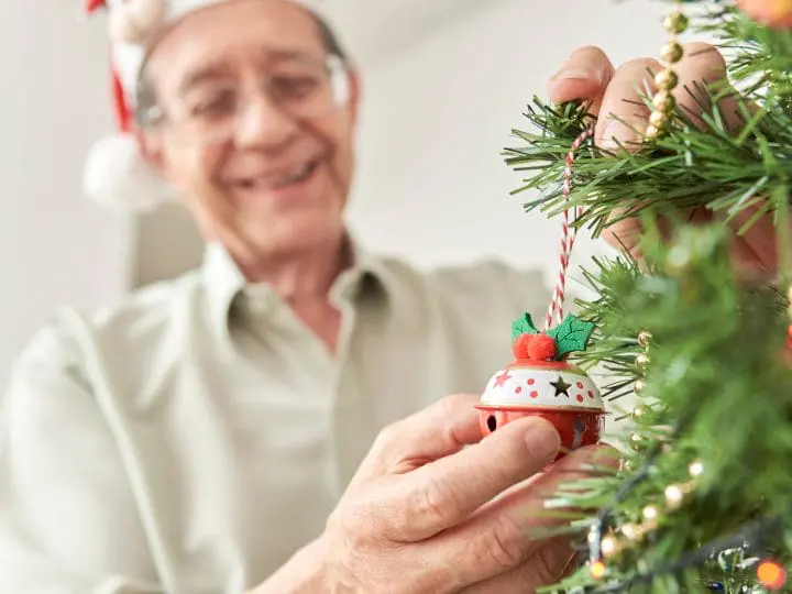 A senior man hangs ornaments on the Christmas tree.