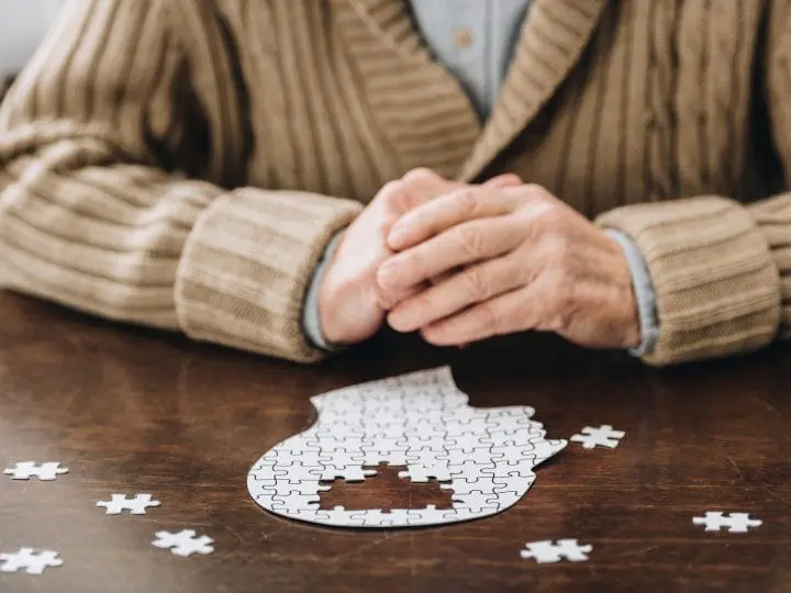 A senior citizen putting together a puzzle in the shape of a head with the center missing, showcasing dementia.