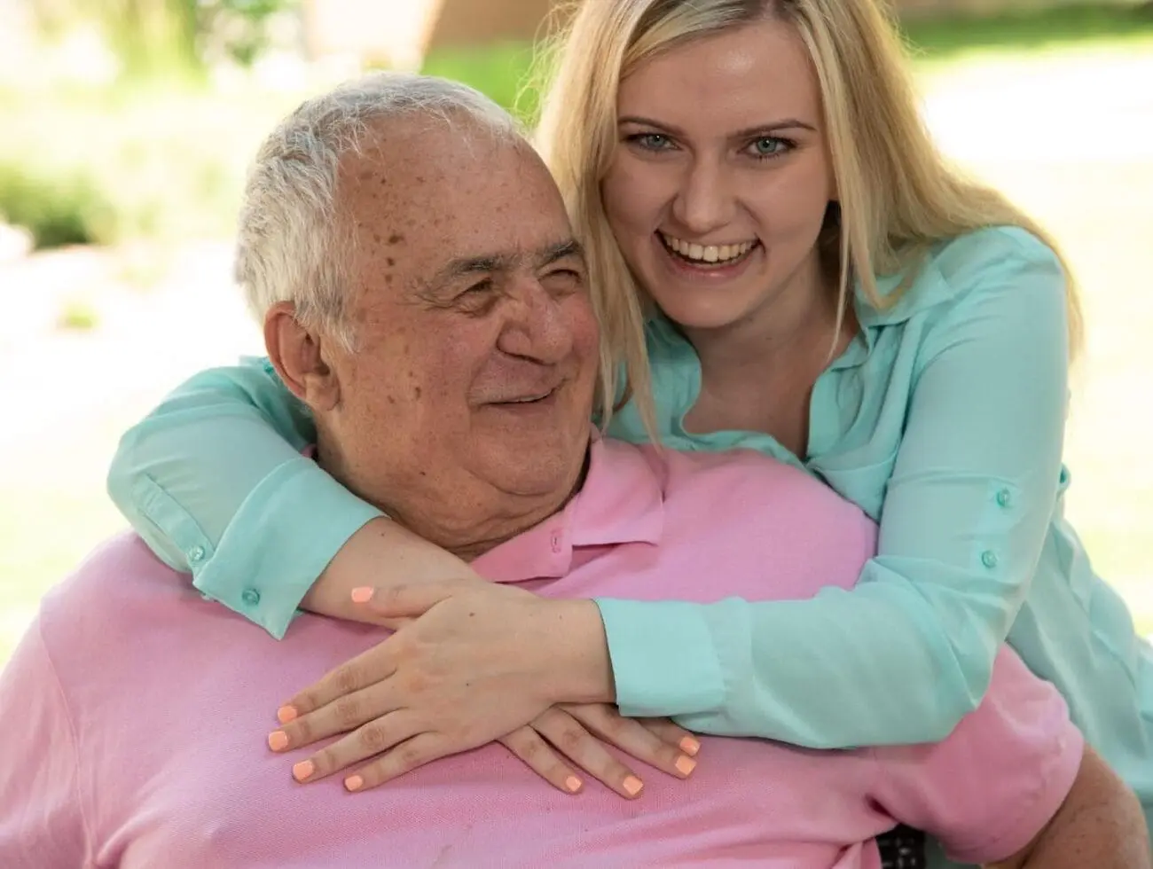 A daughter hugging her elderly father as she visits him in senior living.