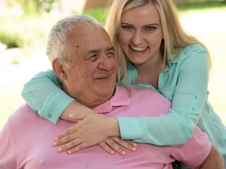 A daughter hugging her elderly father as she visits him in senior living.
