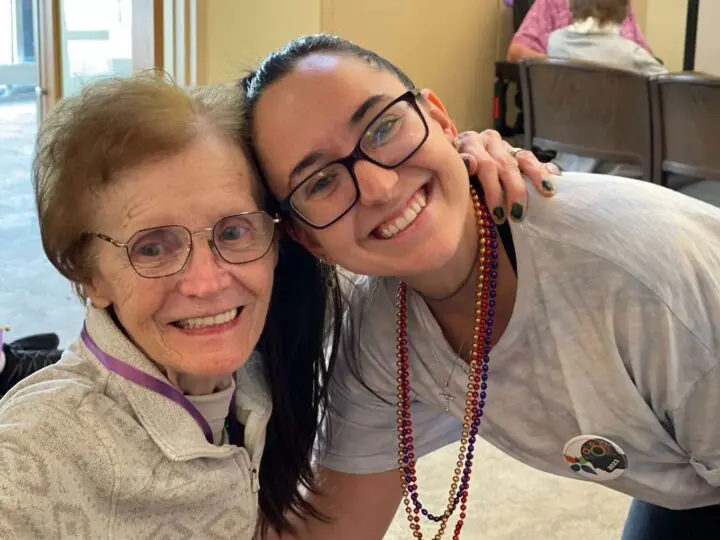 A woman smiles for the camera with her mom who lives in a nursing home.