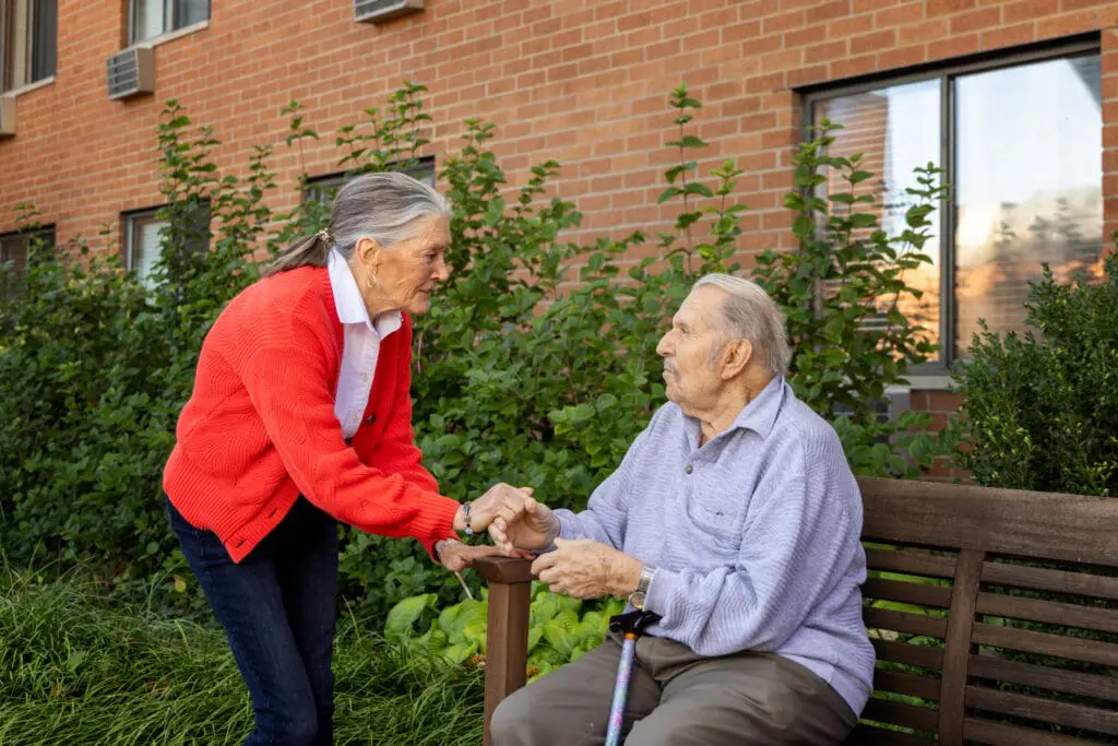 Marty Smith holds the hand of a male resident who is sitting on a bench