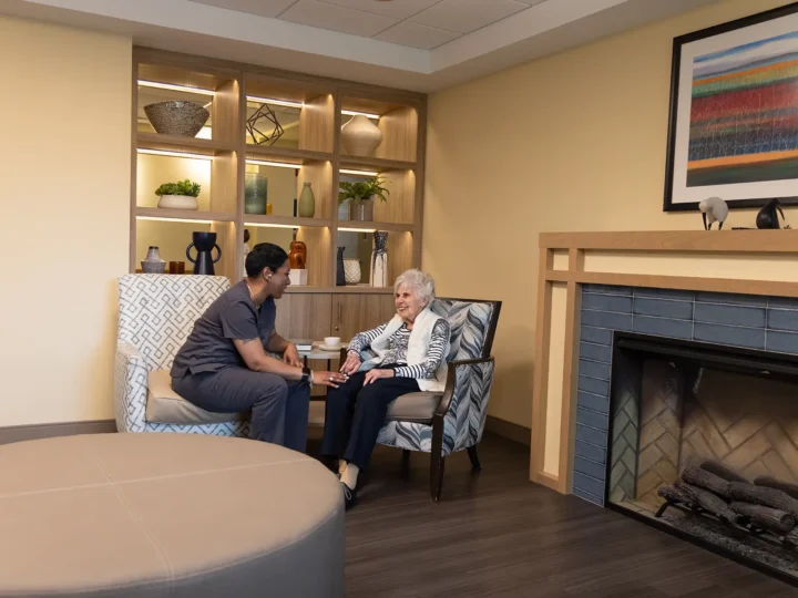 Resident and her caregiver chatting by the fireplace