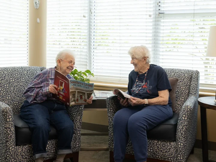 Two residents sitting together and laughing while reading magazines