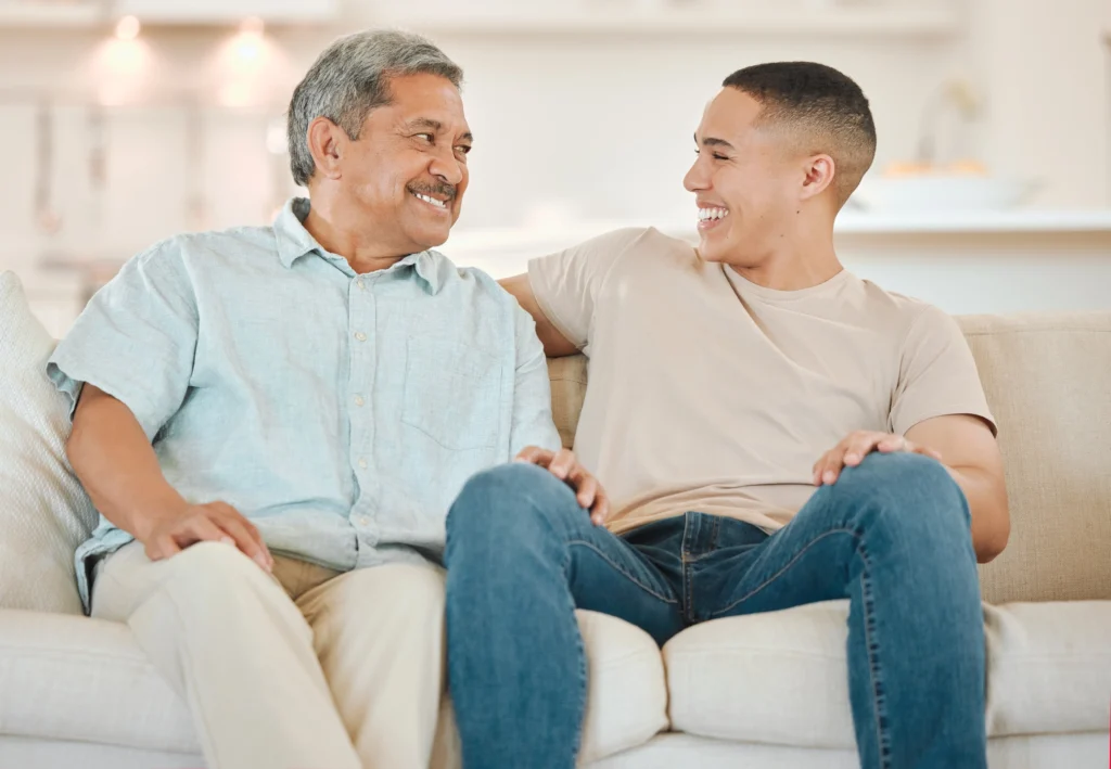 senior man and adult son talking on couch, discussing fun questions to ask someone with dementia in his home at Central Baptist Village at Norridge, Illinois.